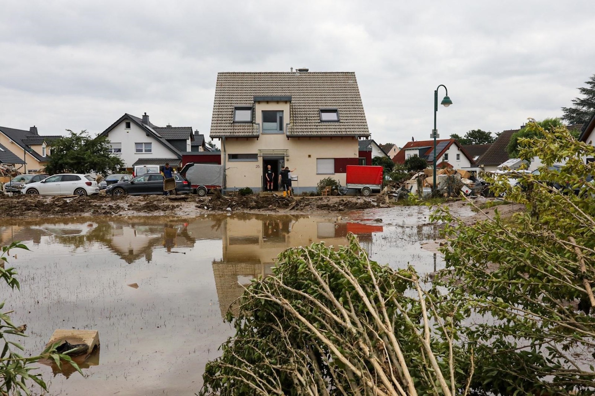 Menschen stehen vor ihrem Haus, das überschwemmt wurde. Im Vordergrund: Schlamm und Müll