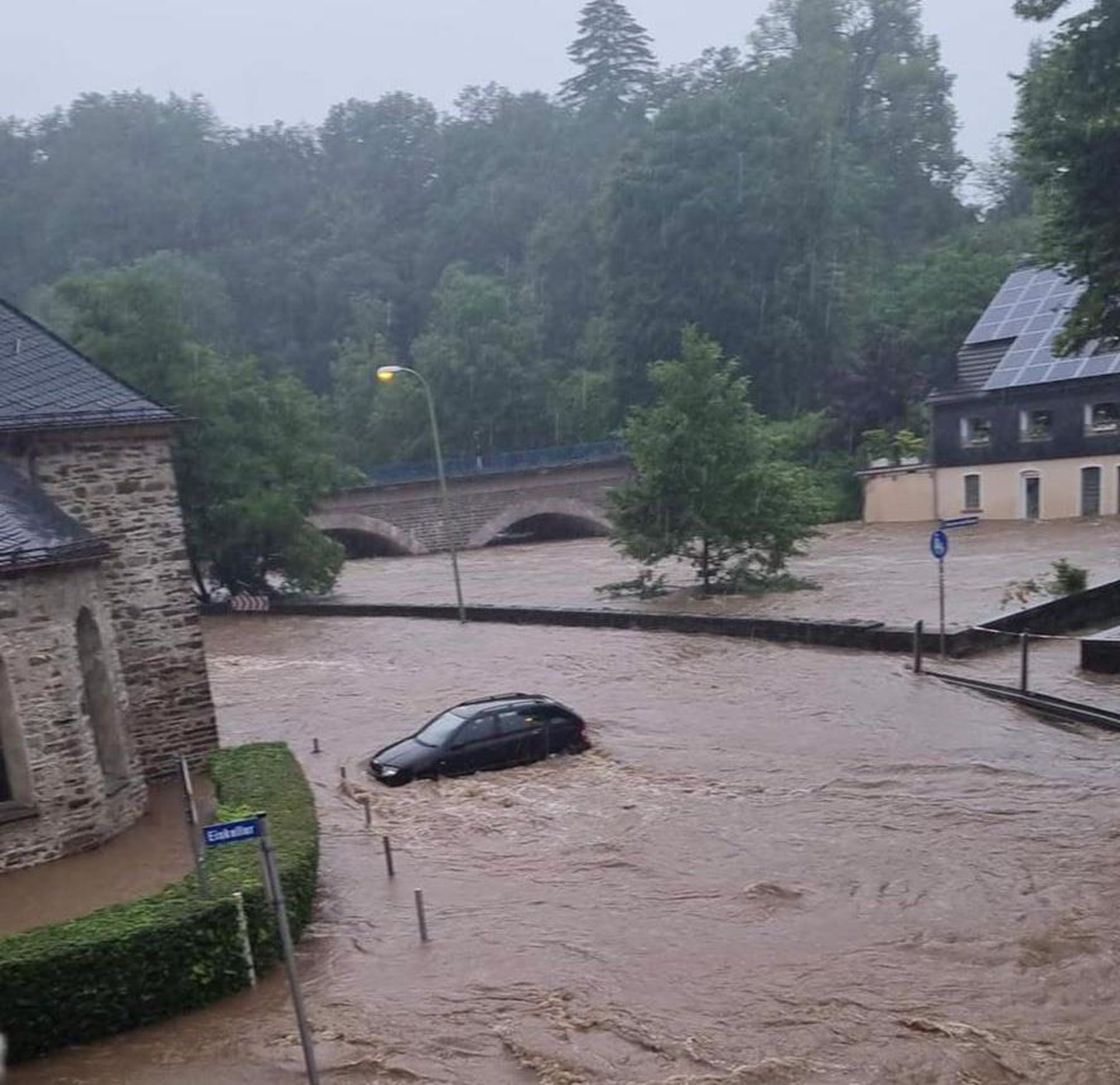 In braunen Wassermassen wird ein Auto weggeschwemmt. Die Straße steht hoch unter Wasser, eine Brücke ist nur noch halb zu sehen